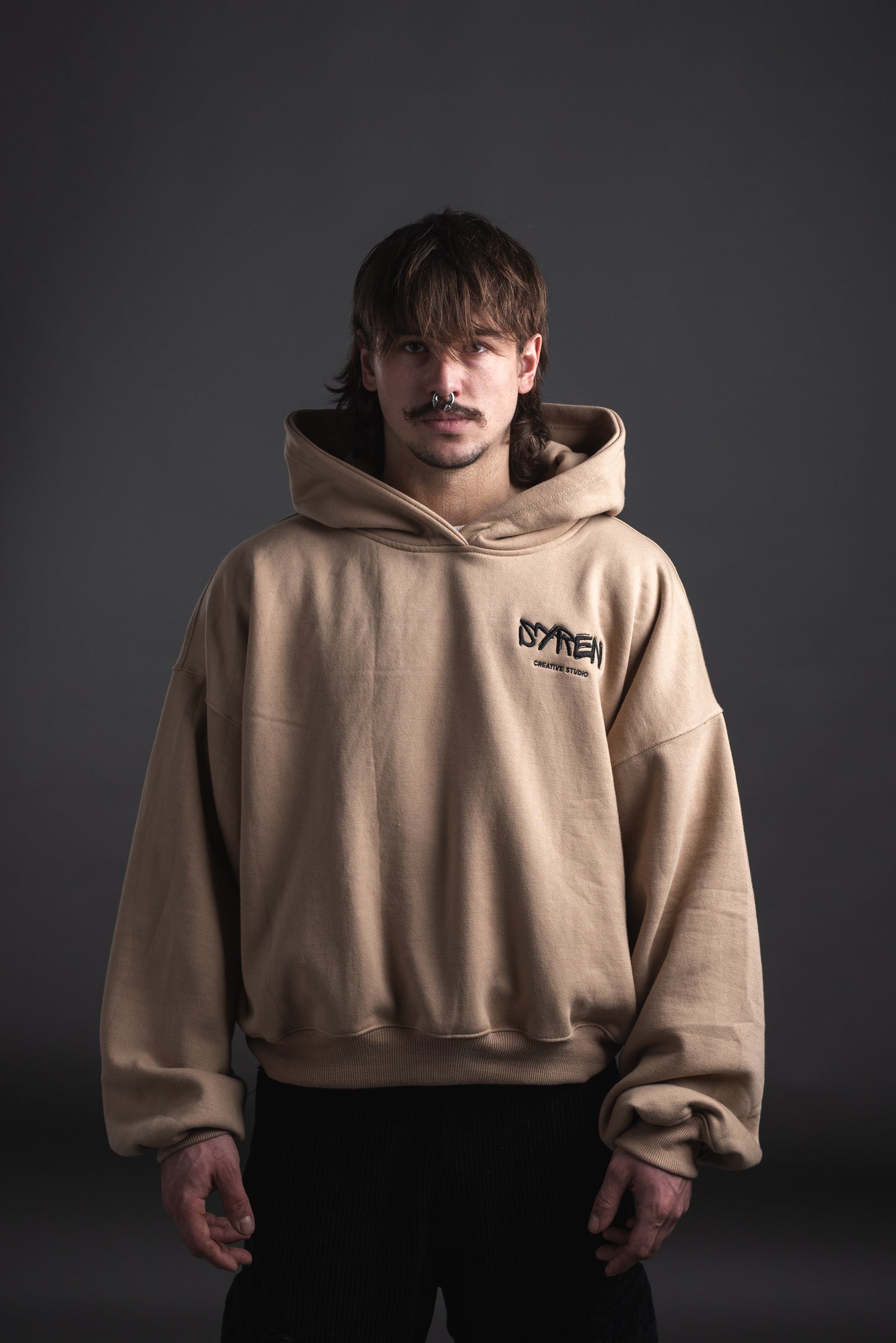 Male model wearing oversized SYREN hoodie in beige – front view